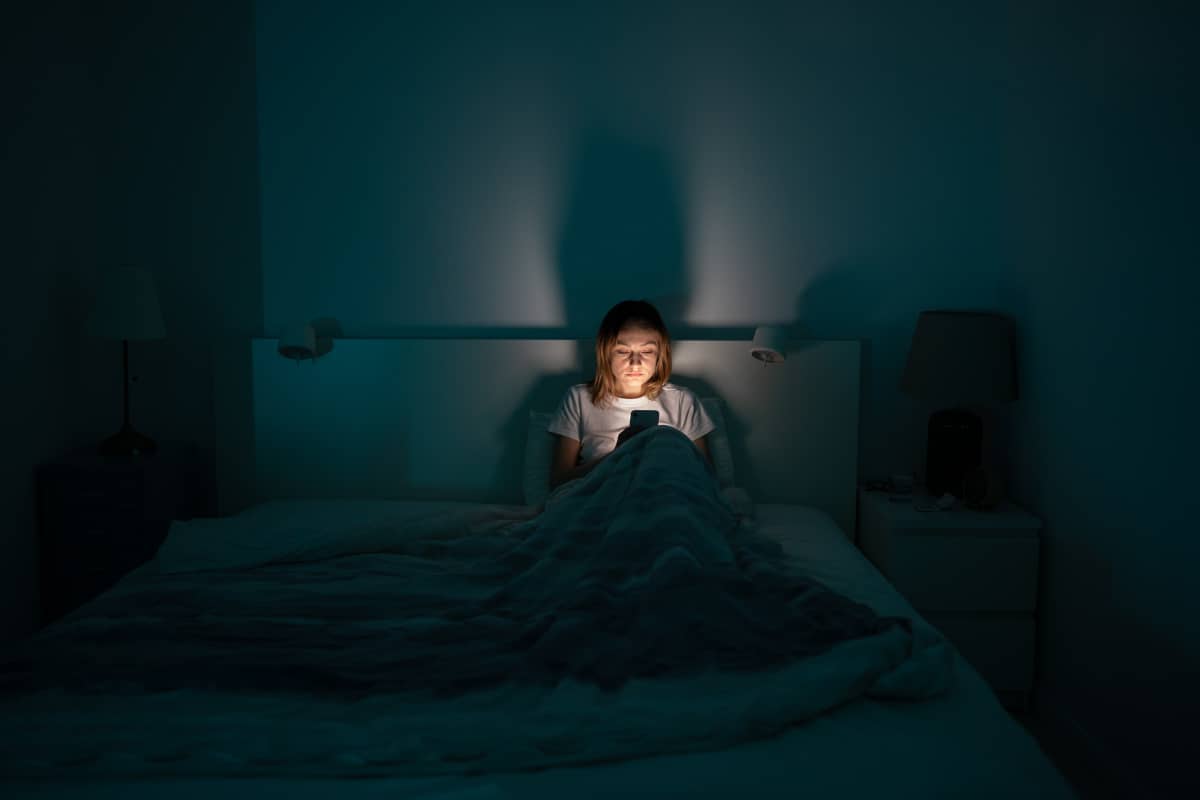 femeie care sufera de insomnie butoneaza telefonul noaptea in pat